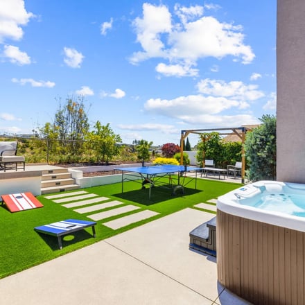 Backyard with hot tub, ping pong and cornhole under blue sky