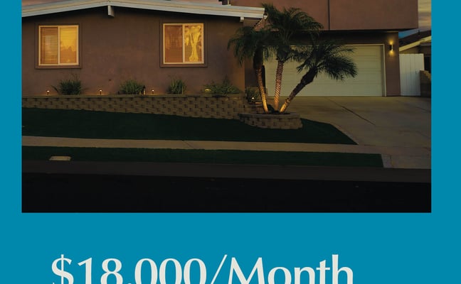 Modern brown two-story house with garage, palm tree, and lit windows at dusk