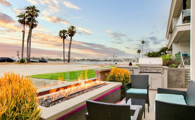 Beachfront patio with fire pit, outdoor kitchen, and sunset view over palm trees and water